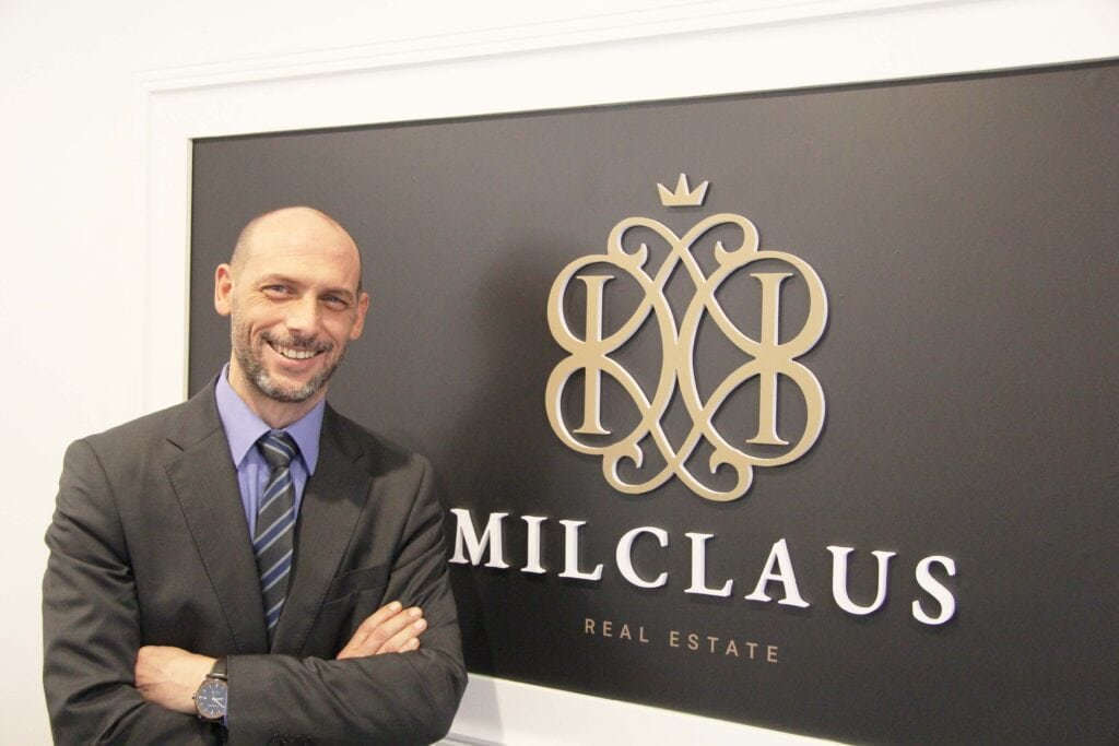 Un hombre de traje parado frente a un cartel de millauus real estate.