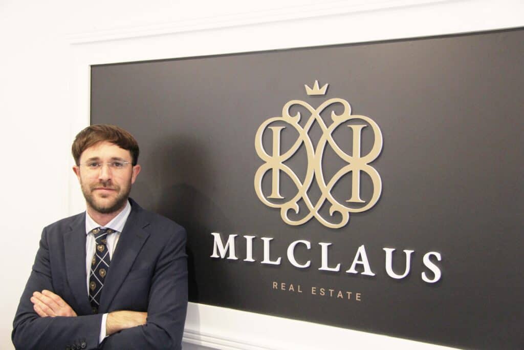 Un hombre de traje parado frente a un cartel que dice millauus real estate.