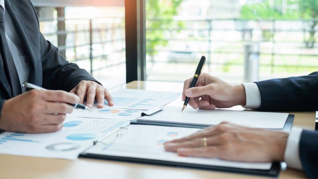 Dos empresarios sentados en una mesa y firmando documentos relacionados con Servicios.