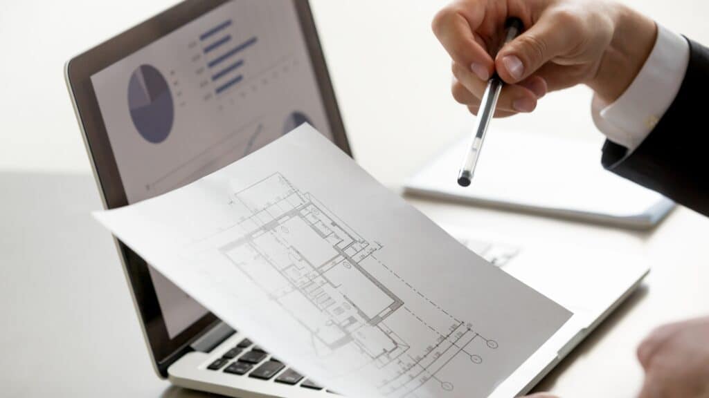 Un individuo está sosteniendo un bolígrafo y consultando un plano en una computadora portátil.Palabras clave: Servicios.